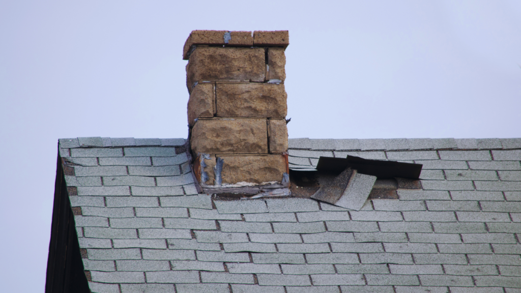 Close-up of a damaged shingle roof with water infiltration near the chimney, highlighting the need for expert roof leak repair