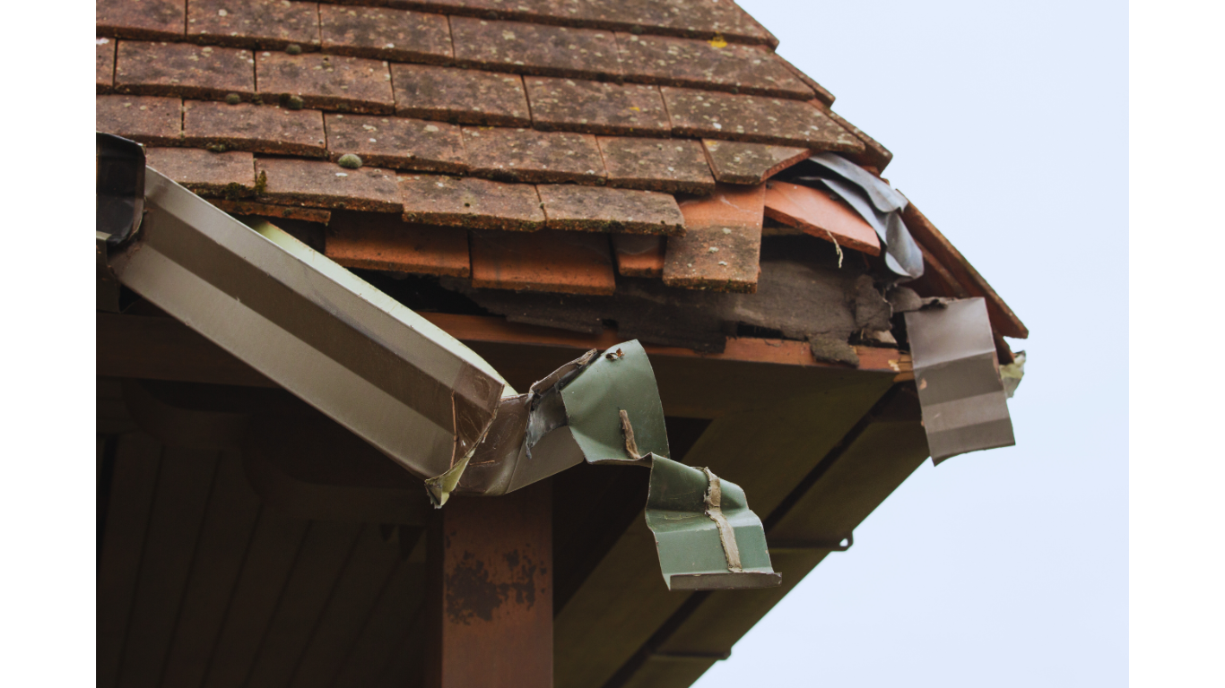 Close-up of a severely damaged and bent metal gutter system on a residential roof, illustrating the need for professional gutter replacement & repair services.