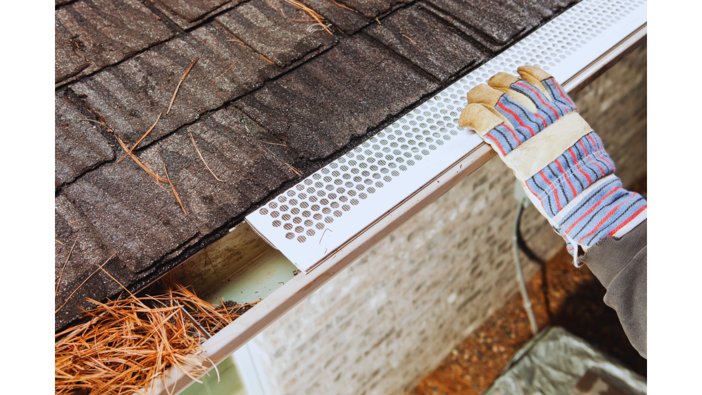 Close-up of a worker installing a metal gutter guard on a residential roof as part of a gutter protection system, preventing leaves and debris from clogging the gutter.