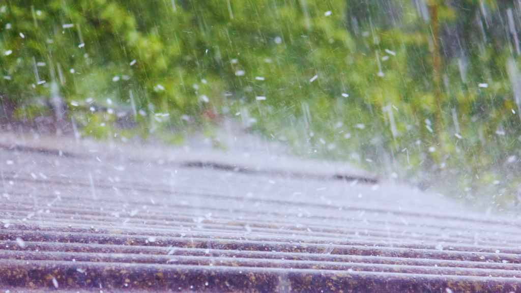 Severe hailstorm hitting a residential roof, causing visible damage that requires professional hail damage roof repair services.