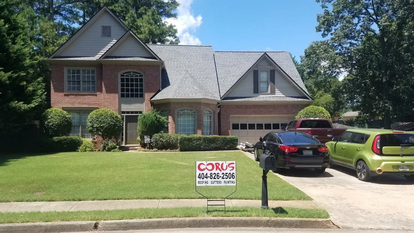 Brick home with newly installed gray roof by the best roofing company in Duluth, GA — Corus Roofing sign displayed in front yard.