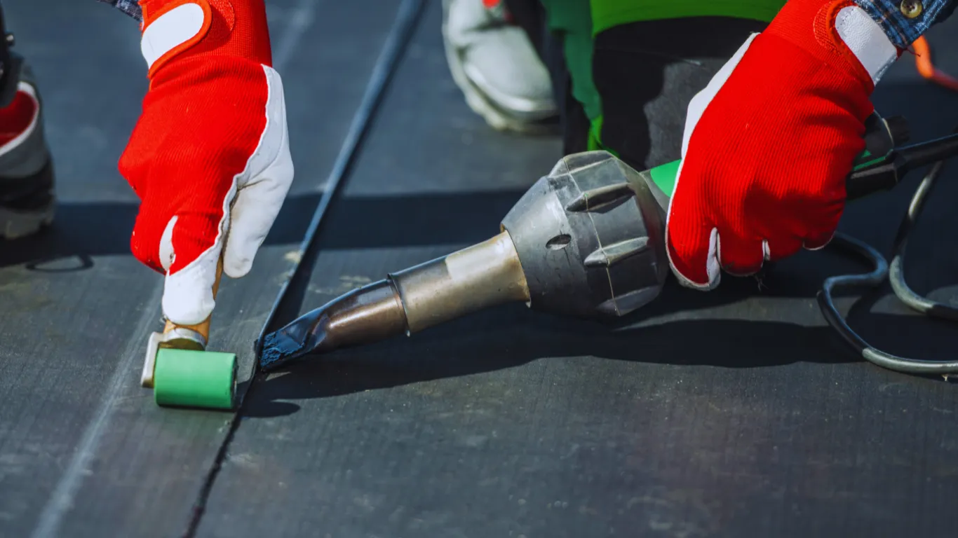 Close-up of contractor using heat welding tool during commercial roof inspection and repair on flat roofing membrane.