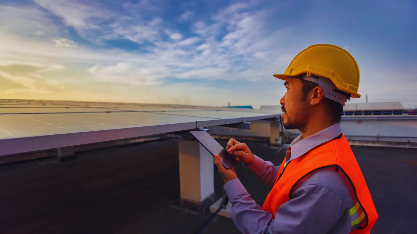Inspector conducting commercial roof inspection with tablet, checking solar panels and rooftop systems at sunset.