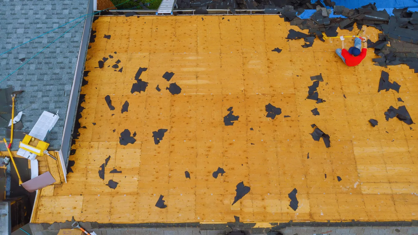 Aerial view of roofing contractor removing old shingles during roof inspection and replacement project on a residential home.