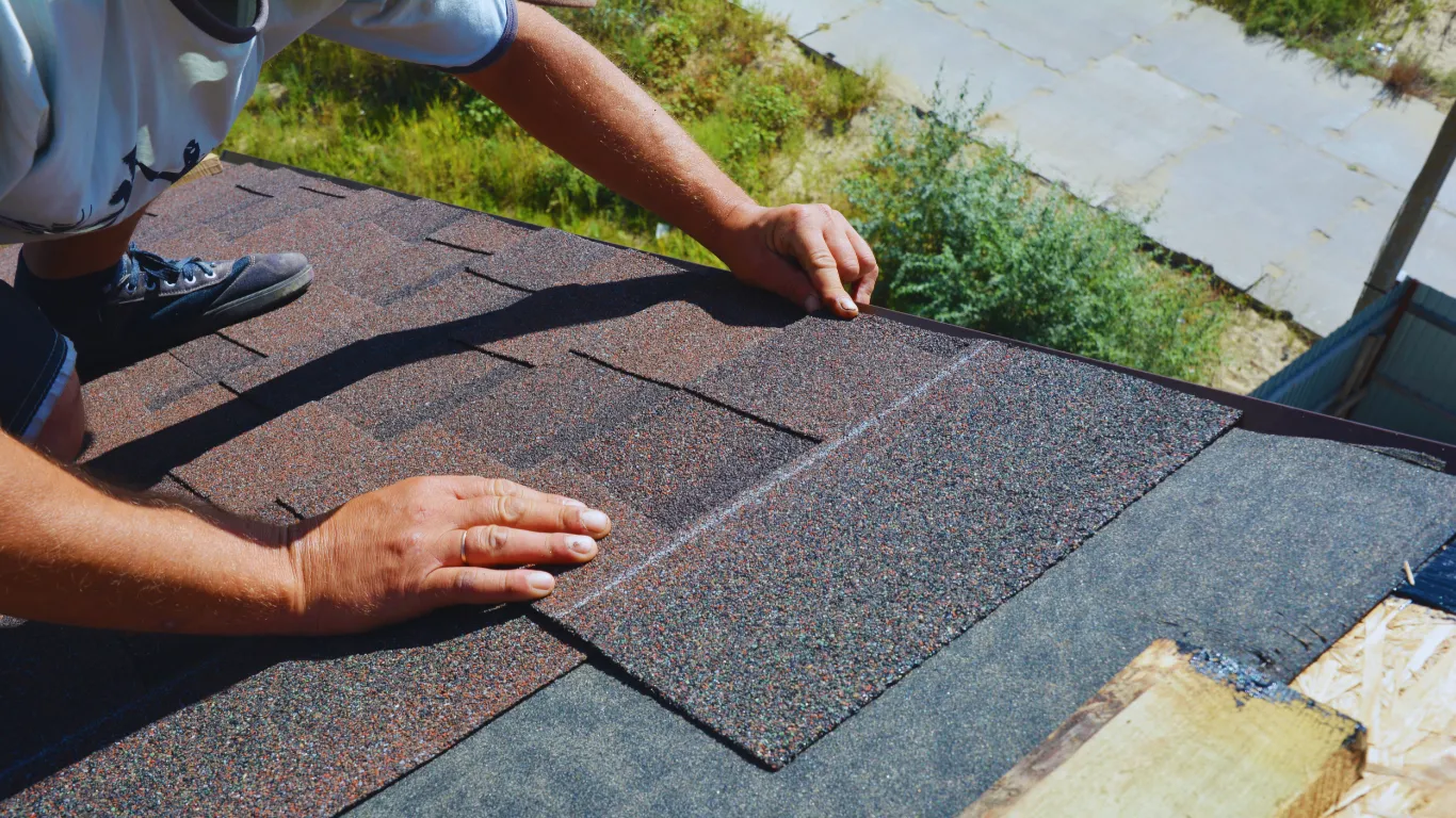 Contractor aligning and installing asphalt shingles during roof inspection and repair to improve durability and weather protection.