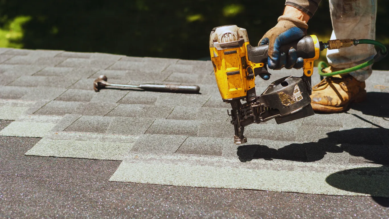 Roofing contractor using nail gun to install new asphalt shingles during roof inspection and replacement for long-term protection.