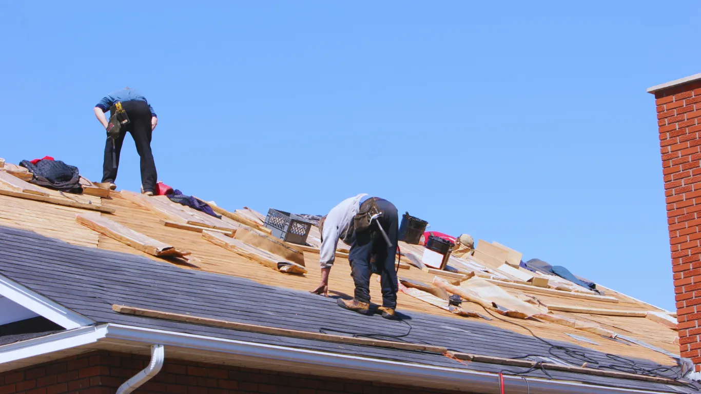 Roofing contractors performing inspection and replacement of shingles on a steep residential roof to ensure safety and durability.